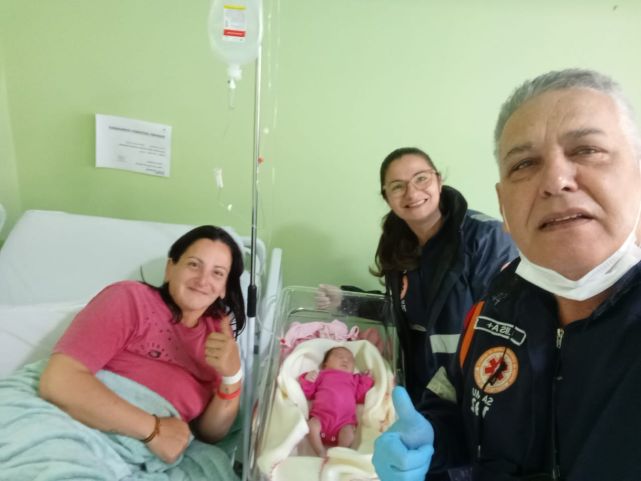 Equipe do Samu em atendimento de emergência obstétrica, profissional verificando sinais vitais de mãe e recém-nascido em ambiente de urgência.