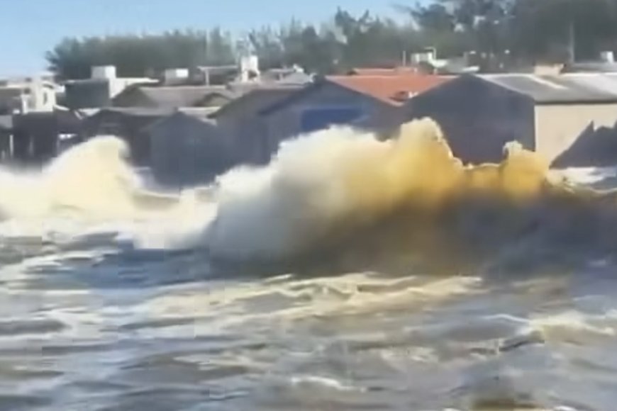 Ondas gigantes quebrando na orla de Laguna durante ciclone-bomba, com espuma branca e mar revolto sob céu nublado.