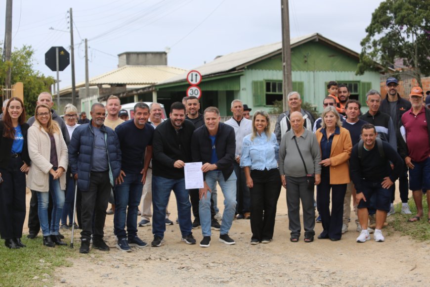 Silhueta de autoridades e moradores assinando documento de ordem de serviço para obra de infraestrutura na Rua José Quintino Corrêa, Alto Arroio.