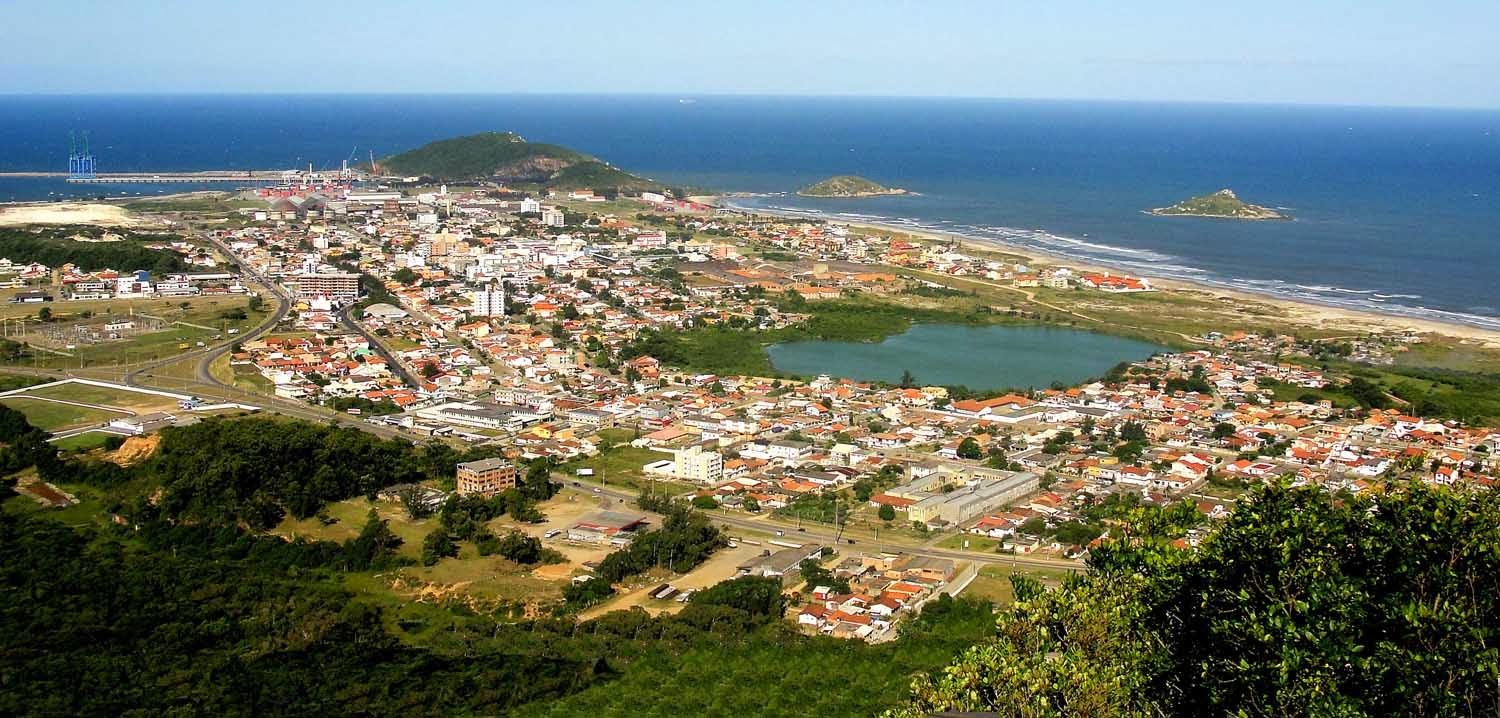 Ilustração editorial flat do centro de Imbituba com silhuetas de casas açorianas, palmeiras e o Porto ao fundo; bandeira do município estilizada em destaque, em tons navy e dourado, celebrando os 68 anos de emancipação.