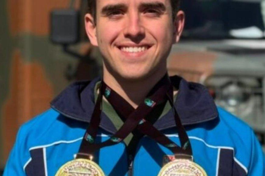 Silhueta azul-marinho de atleta de karatê executando um golpe, com duas medalhas douradas suspensas ao lado e mapa abstrato do Brasil ao fundo sobre fundo off-white.