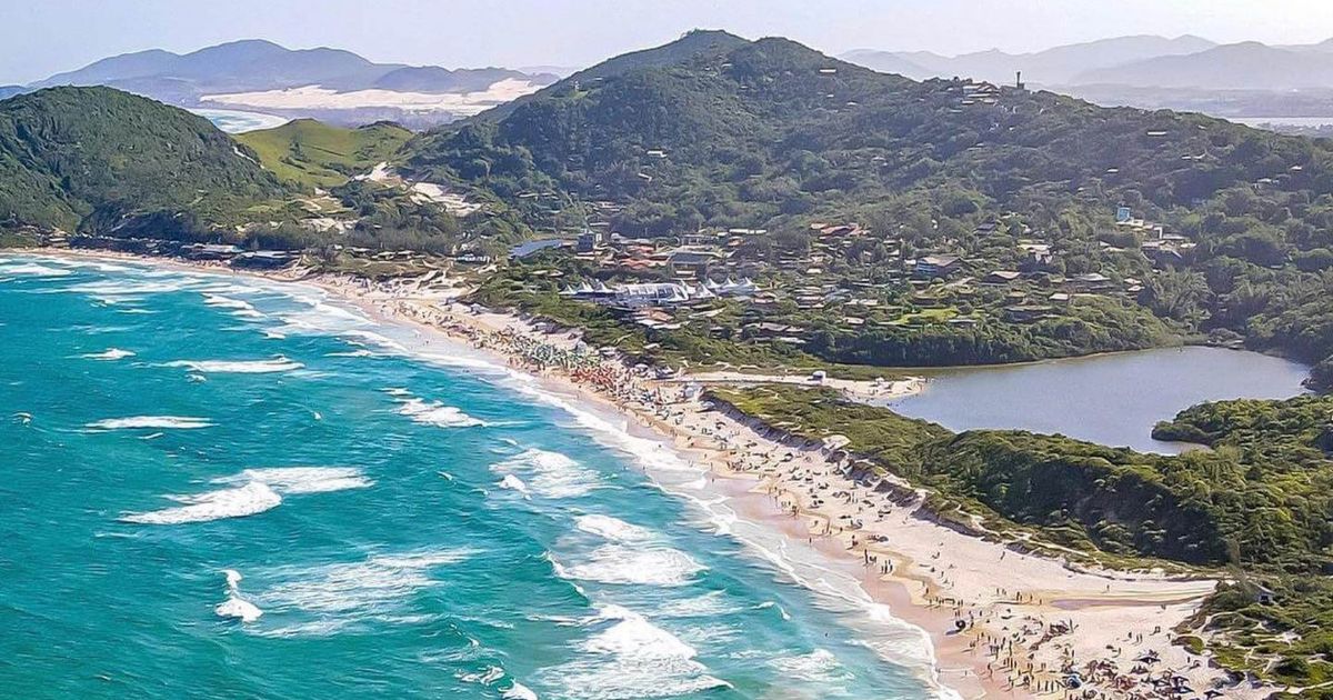 Estrada de acesso a Imbituba com buracos e deterioração visível, contrastando com movimento de turistas e veículos em dia ensolarado.